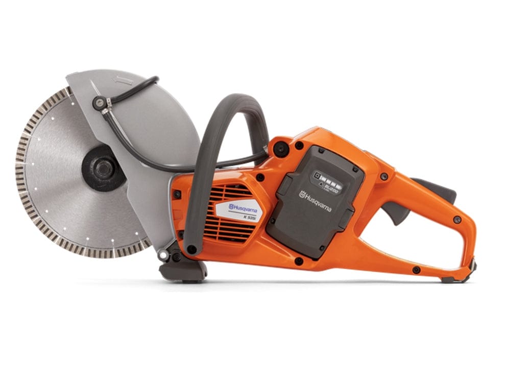Side profile of the Husqvarna K535i cordless cut-off saw with a diamond blade. The battery slot cover is closed, showing the overall compact design and the water feed system.