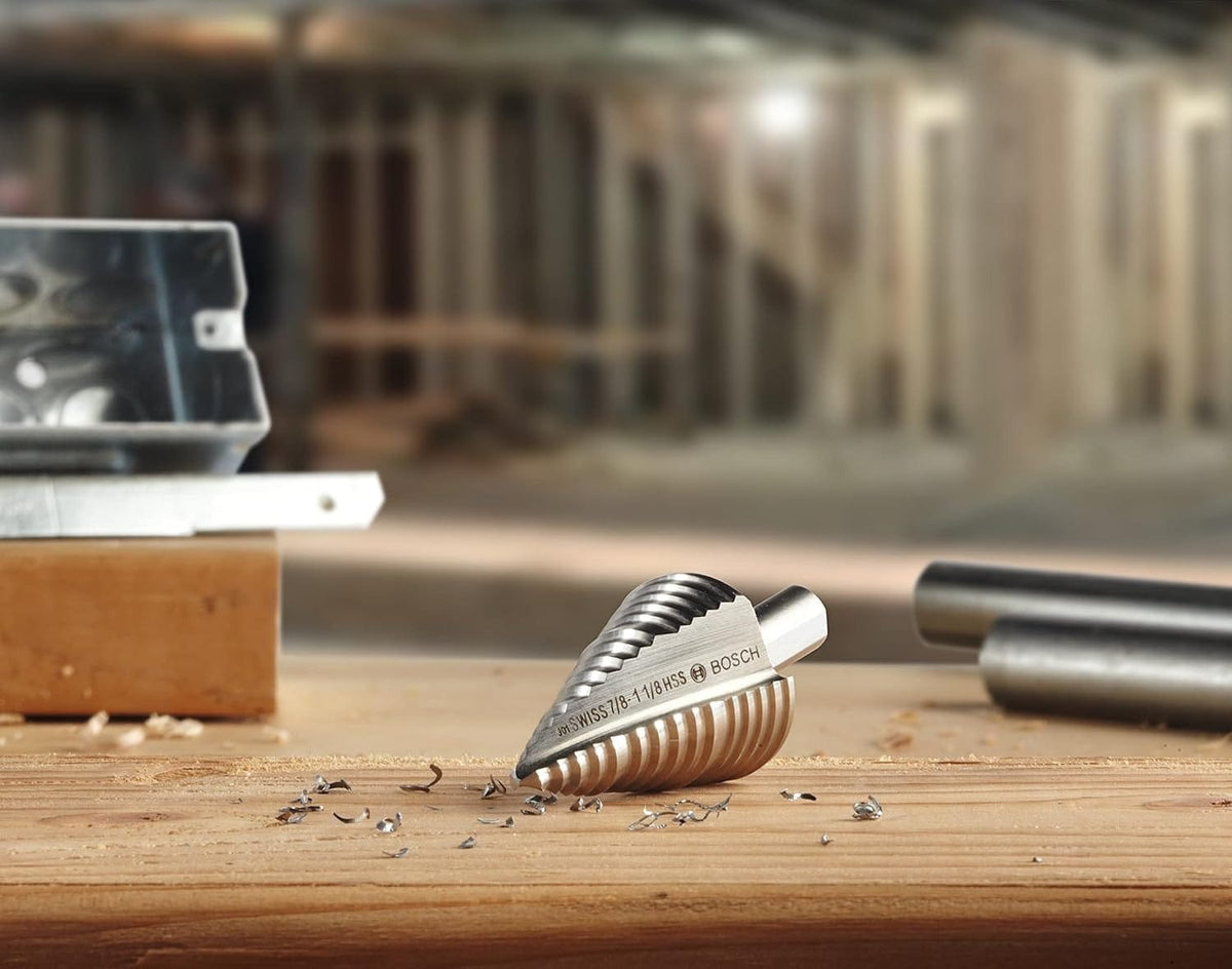 A Bosch HSS Turbo step drill bit rests on a wooden workbench surrounded by metal shavings, with a construction site in the background.