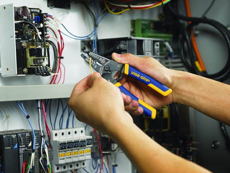 Action shot of a worker's hands using the Irwin Vise-Grip 6-inch adjustable wire stripper and cutter to safely and precisely strip a yellow wire in front of an open electrical control panel