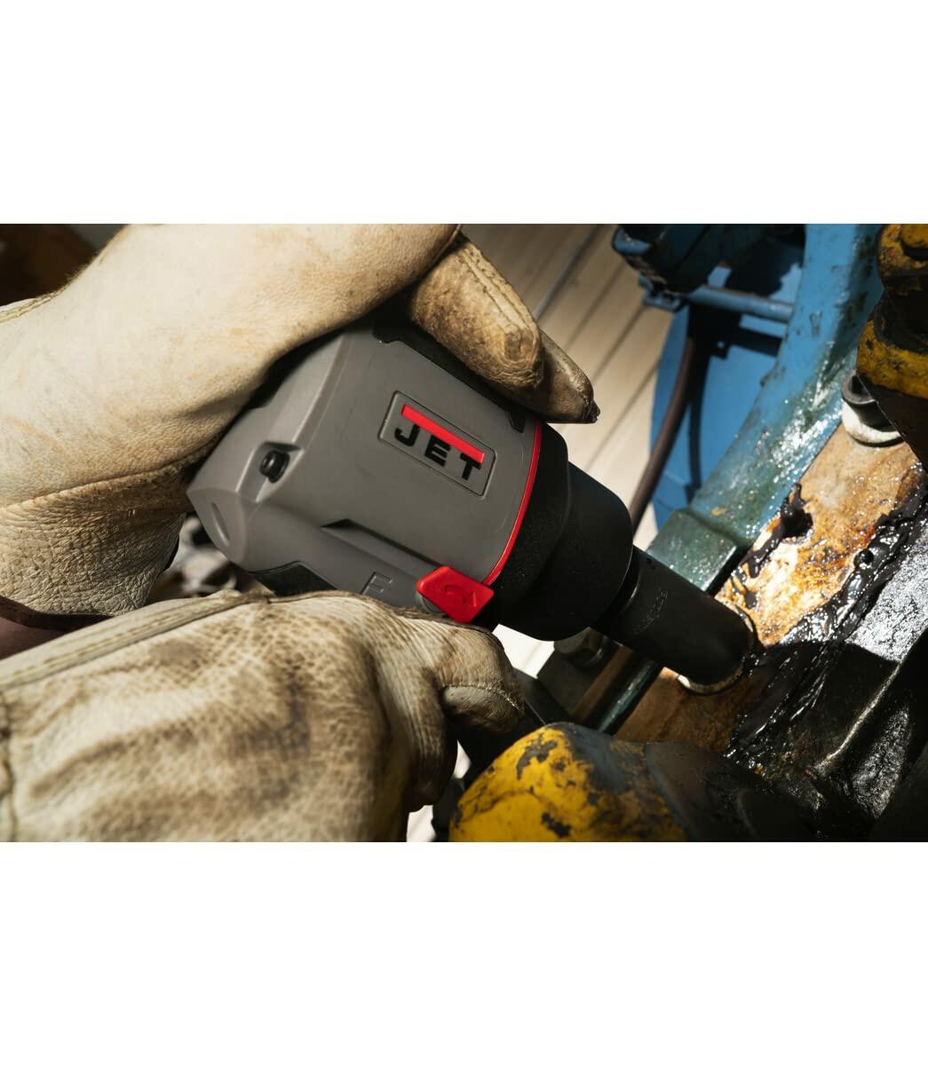 Action shot showing a worker using the compact JET impact wrench in a tight space to work on a dirty, industrial component. The worker is wearing leather gloves.