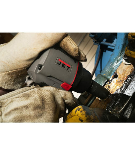 Action shot showing a worker using the compact JET impact wrench in a tight space to work on a dirty, industrial component. The worker is wearing leather gloves.
