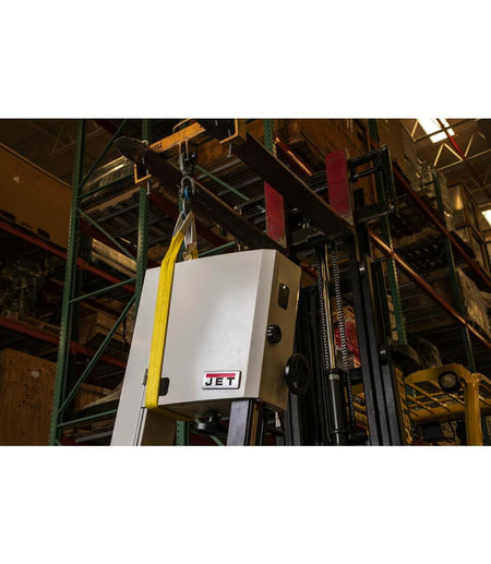A yellow JET polyester web sling attached to a forklift's lifting accessory, being used to lift a piece of JET machinery in a warehouse environment.