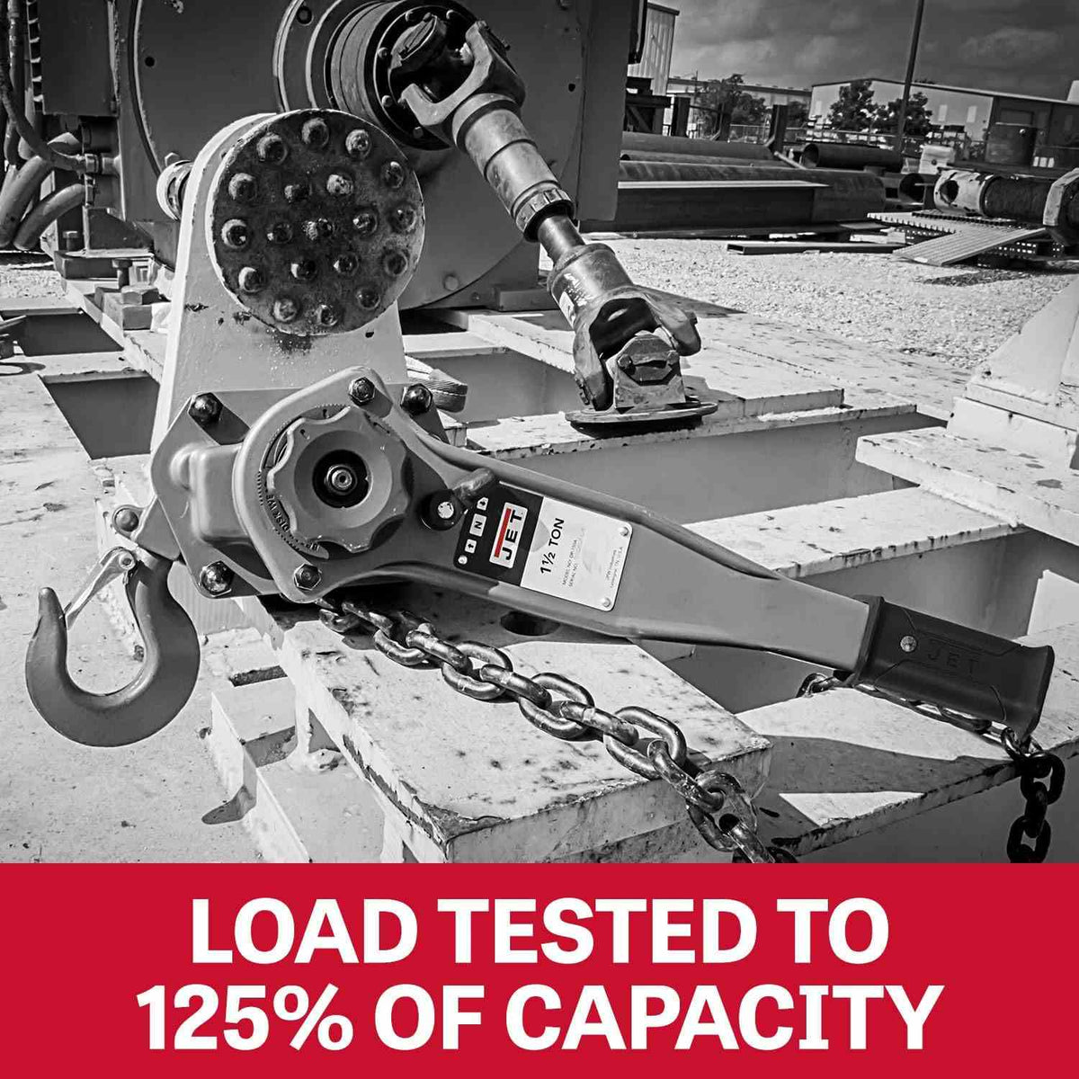 Black and white photo of the lever hoist anchored to heavy machinery, highlighting that the unit is load tested to 125 percent of capacity.