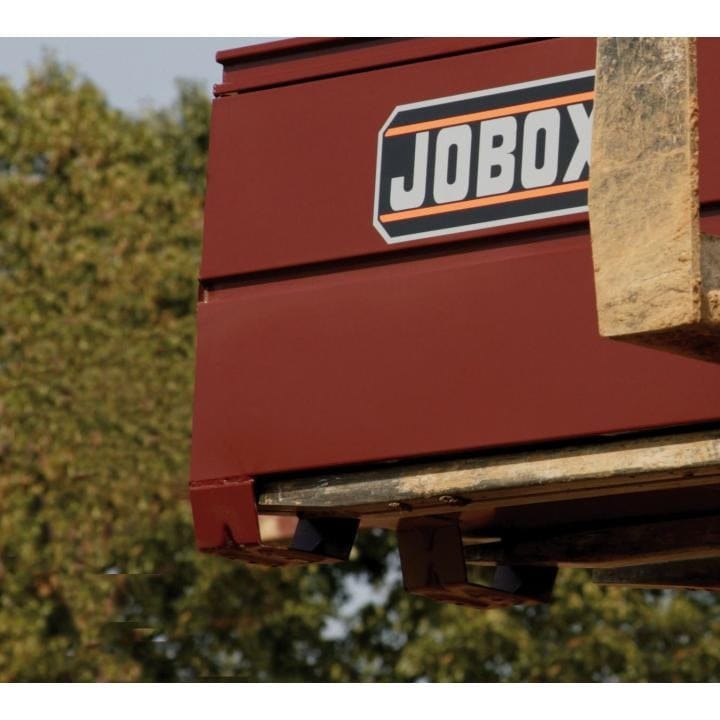Side view of a red JOBOX steel cabinet being lifted outdoors by heavy machinery, showing the brand logo and rugged construction.