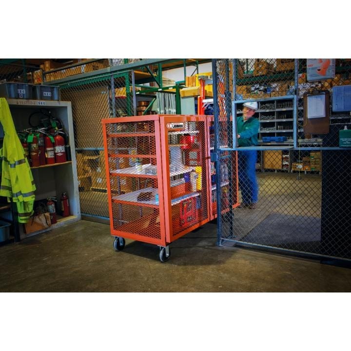 Red JOBOX mesh storage cart in a fenced warehouse area, filled with tools and supplies; nearby fire extinguishers and a worker in safety gear are visible