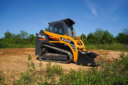 KATO CL35 compact track loader parked on dirt with bucket attachment and rubber tracks, shown in outdoor setting with trees and blue sky in background.