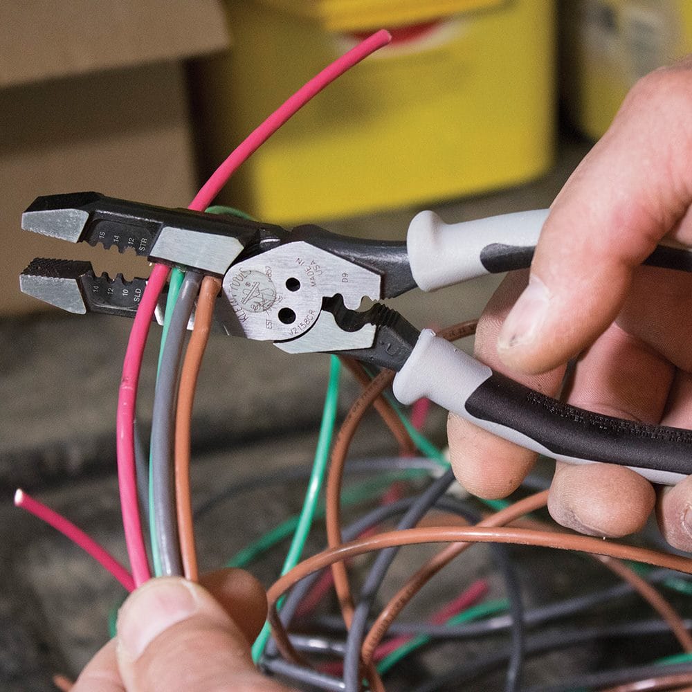 An action shot of the Klein J215-8CR hybrid pliers being used to strip the insulation from a green wire, surrounded by other wires.