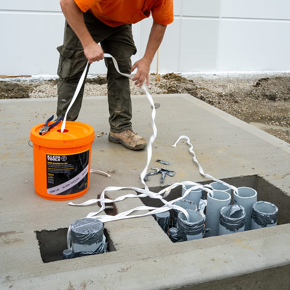 Contractor pulling pre-lubricated polyester tape out of the bucket dispensing hole into multiple commercial electrical conduit openings.
