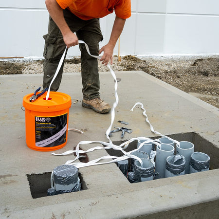 Contractor pulling pre-lubricated polyester tape out of the bucket dispensing hole into multiple commercial electrical conduit openings.