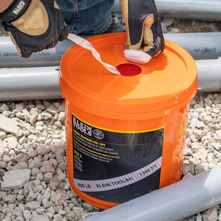Close-up of a worker pulling white pre-lubricated measuring tape through the bucket lid access aperture on a gravel construction site.