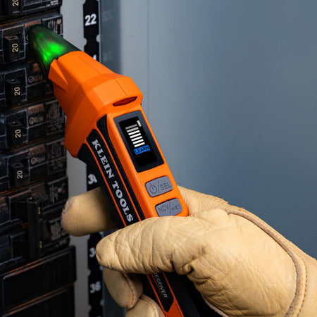 Gloved electrician holding the Klein ET350 receiver wand in Learn Mode while scanning individual breaker switches in an electrical panel.