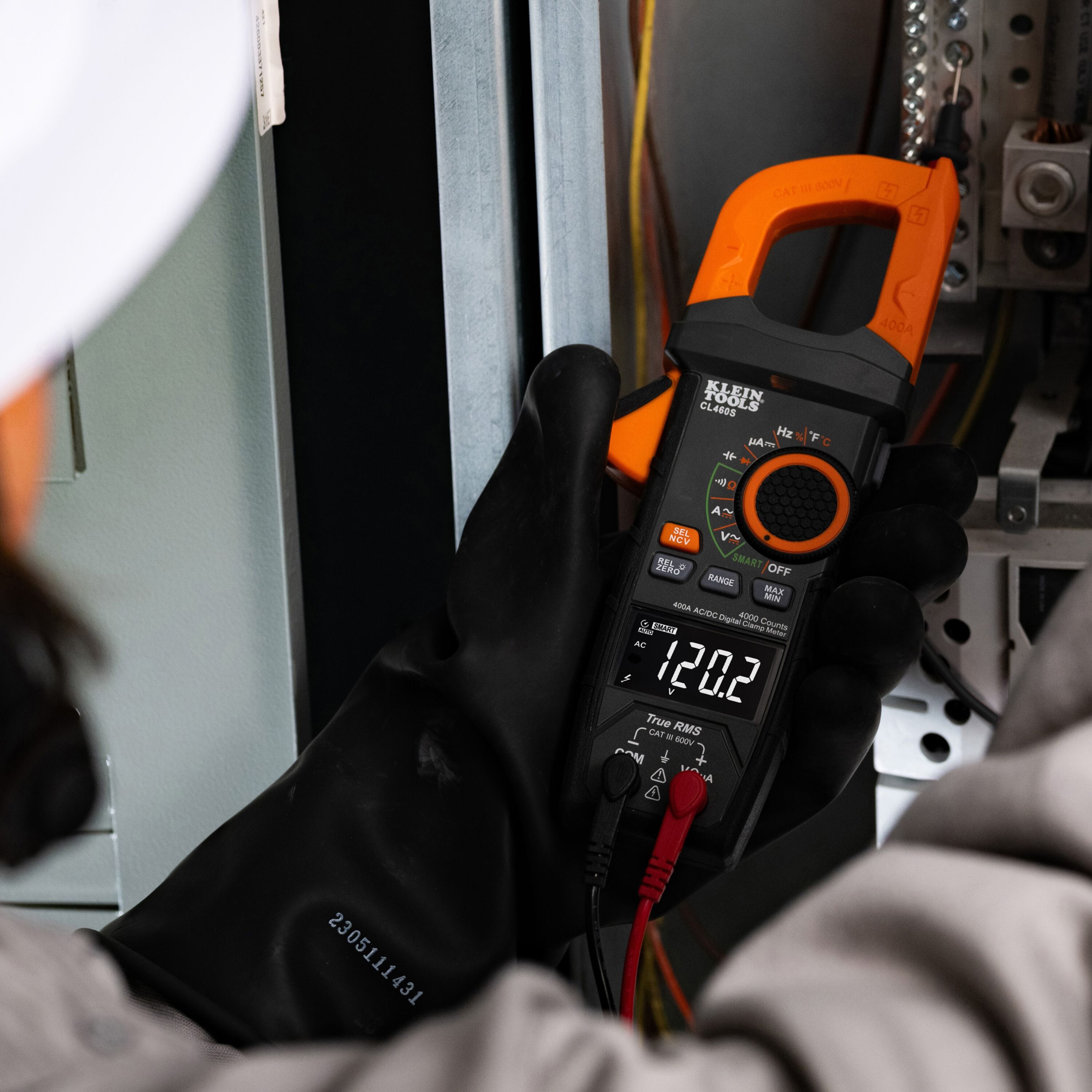 Electrician wearing insulated high-voltage gloves using the Klein CL460S test leads to measure live AC voltage inside an electrical panel.