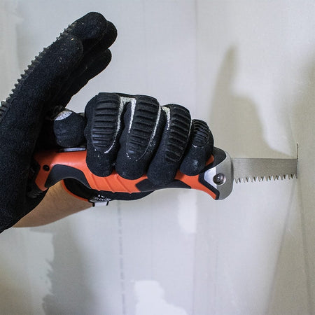 A close-up action shot of a gloved hand gripping the Klein jab saw to make a cut in drywall.