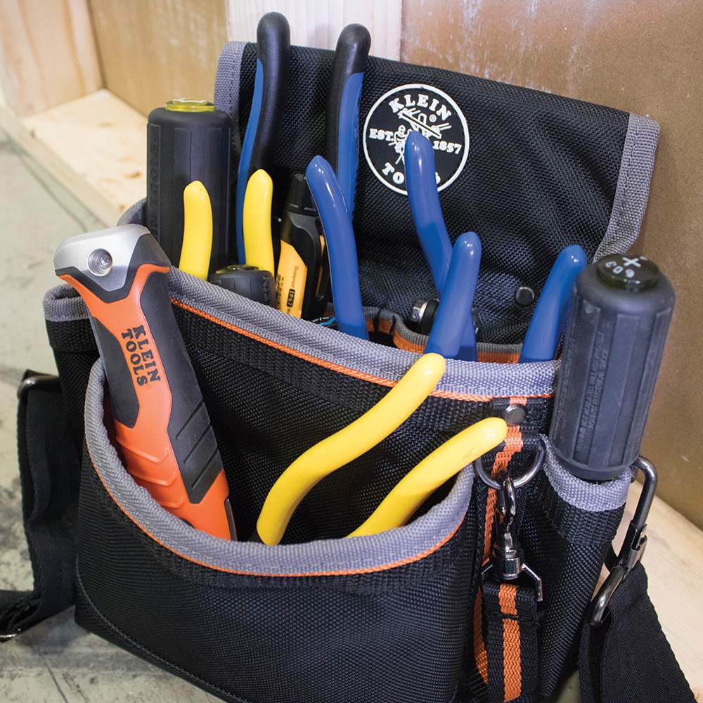 The Klein folding jab saw shown folded and stored in the pocket of a black Klein Tools tool pouch, alongside other tools.
