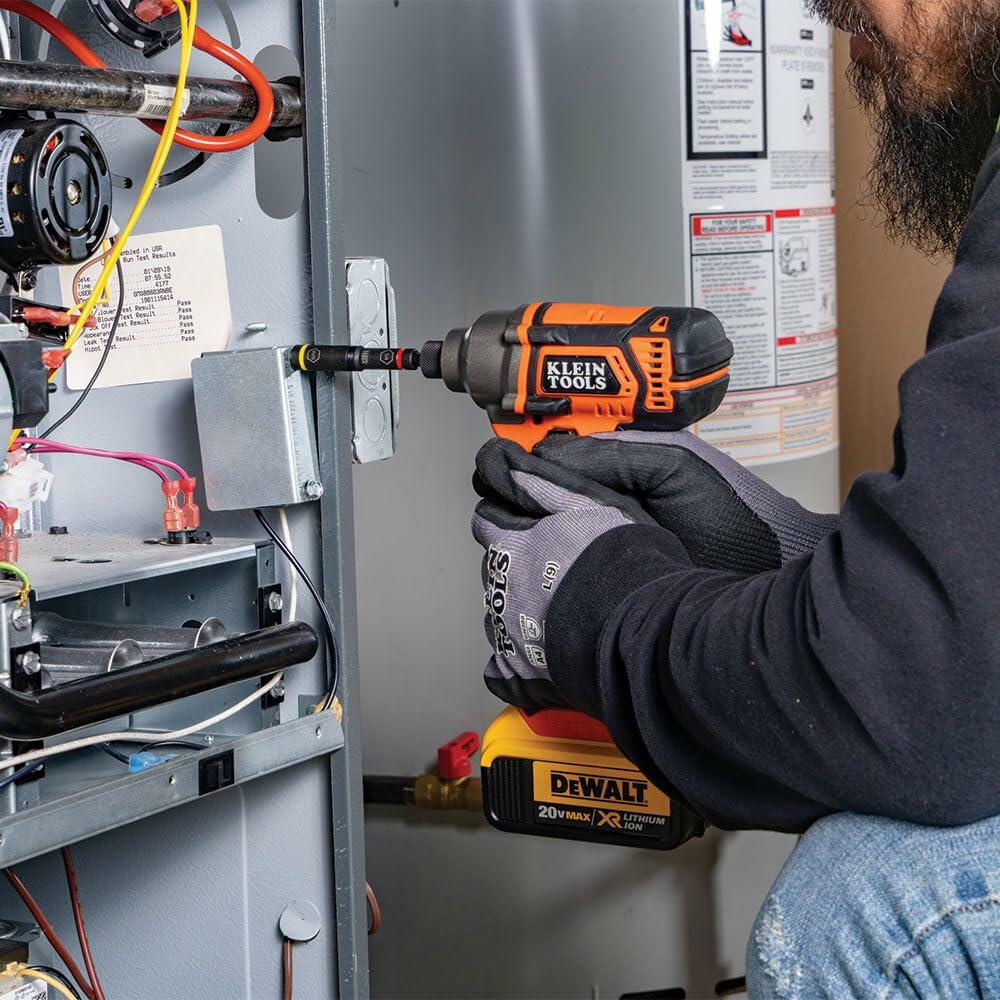 A worker using an orange and black impact driver (Klein KNECT system compatible) with a KNECT adapter and socket to drive a fastener into an electrical box mounted on a furnace or HVAC unit.