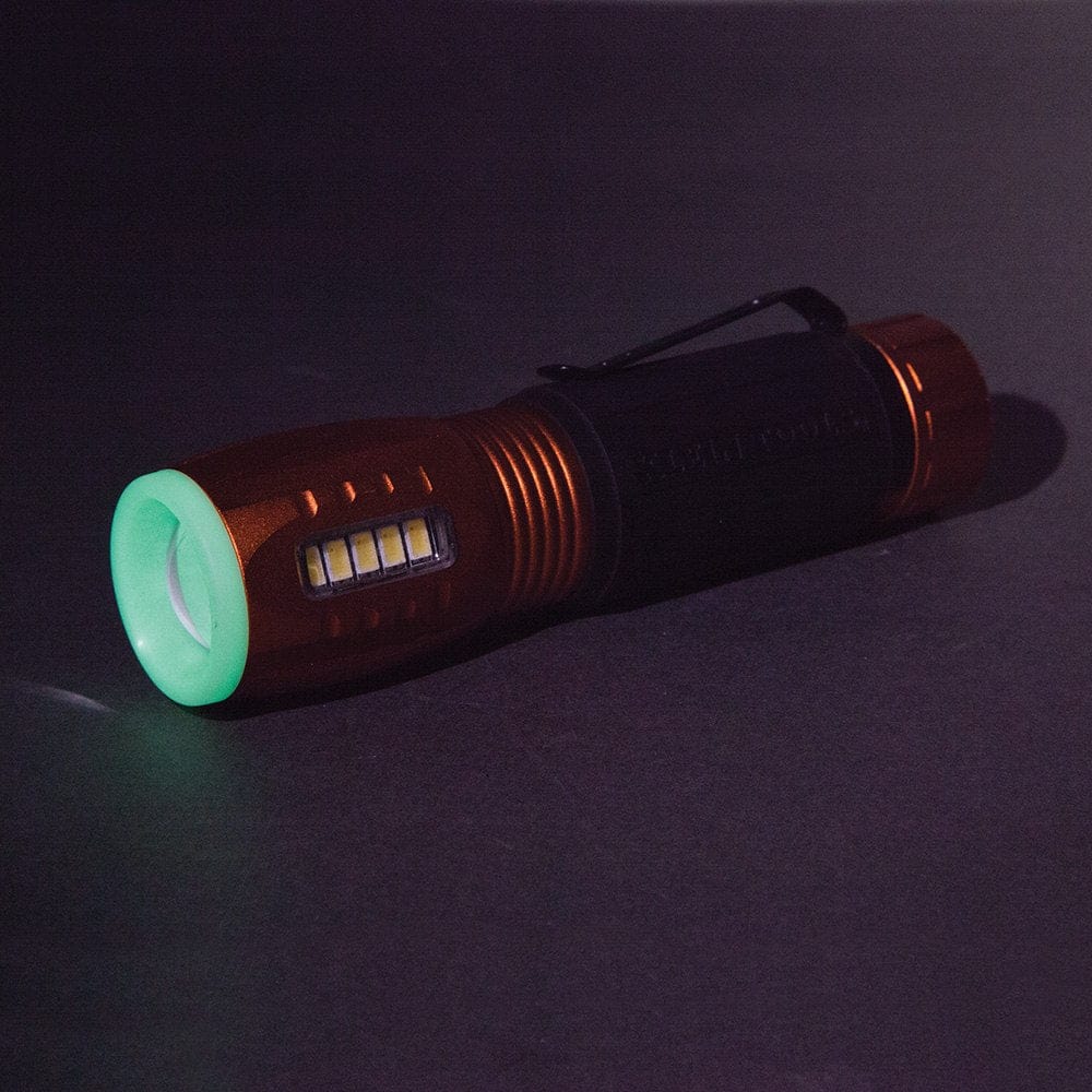 The Klein 56028 flashlight is shown in a dark setting, with its glow-in-the-dark tip shining a bright green.