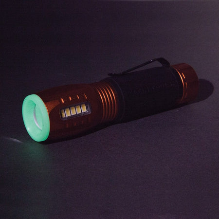 The Klein 56028 flashlight is shown in a dark setting, with its glow-in-the-dark tip shining a bright green.
