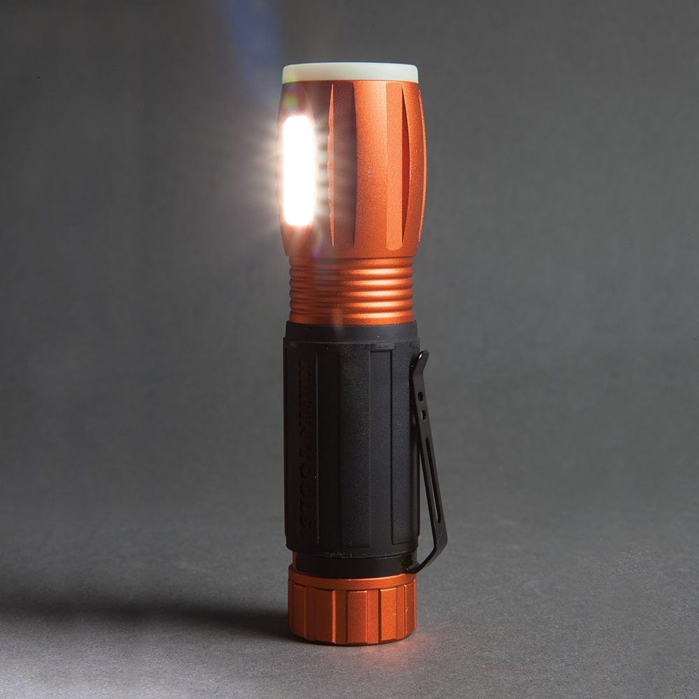 A studio shot of the Klein 56028 flashlight standing upright, with its side work light on and its main beam pointing upward.