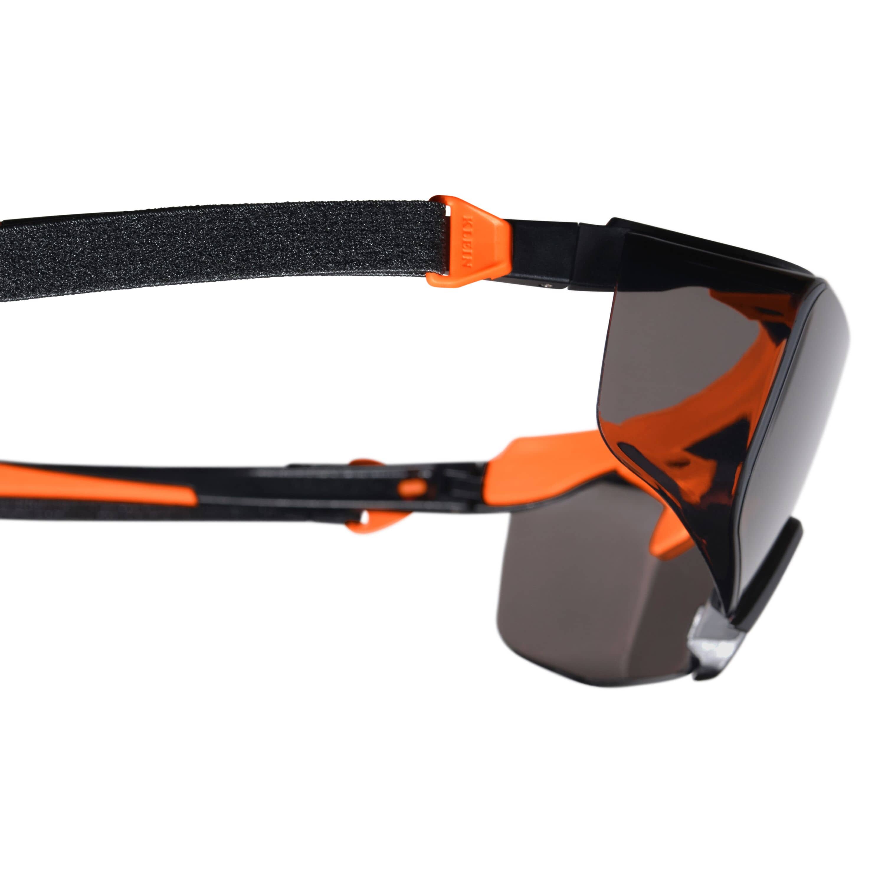 Close-up side profile of the safety glasses showing the gray shaded lens and the integrated attachment point for the black fabric security strap on the orange and black nylon stems.