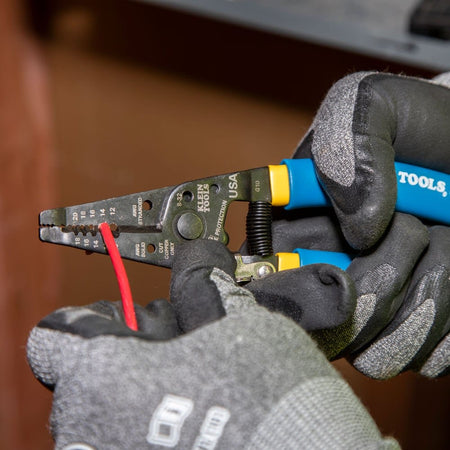 Close-up of gloved hands using the cutting blades of the tool to shear through a red wire.