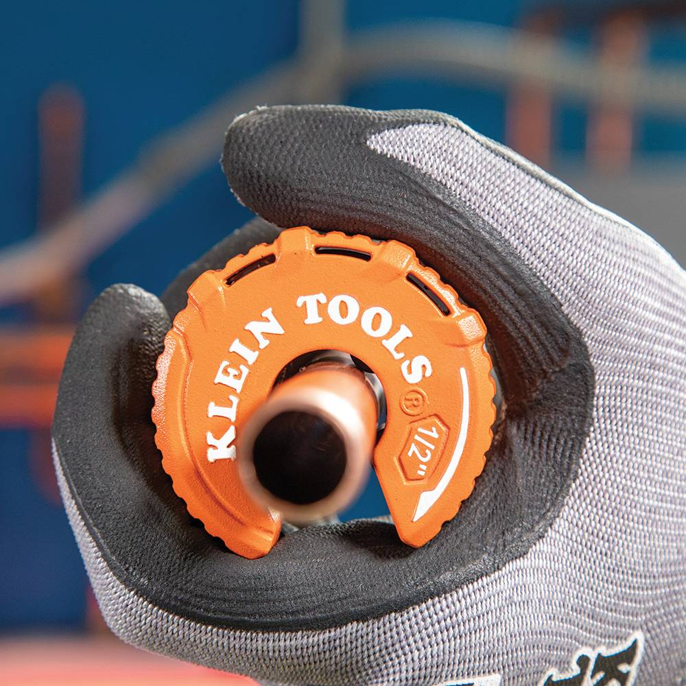 A first-person perspective of a professional plumber holding the Klein Tools 50055 cutter while it is engaged around a copper pipe. The ribbed grip allows for easy rotation, showcasing the ergonomic design for repetitive job site use.