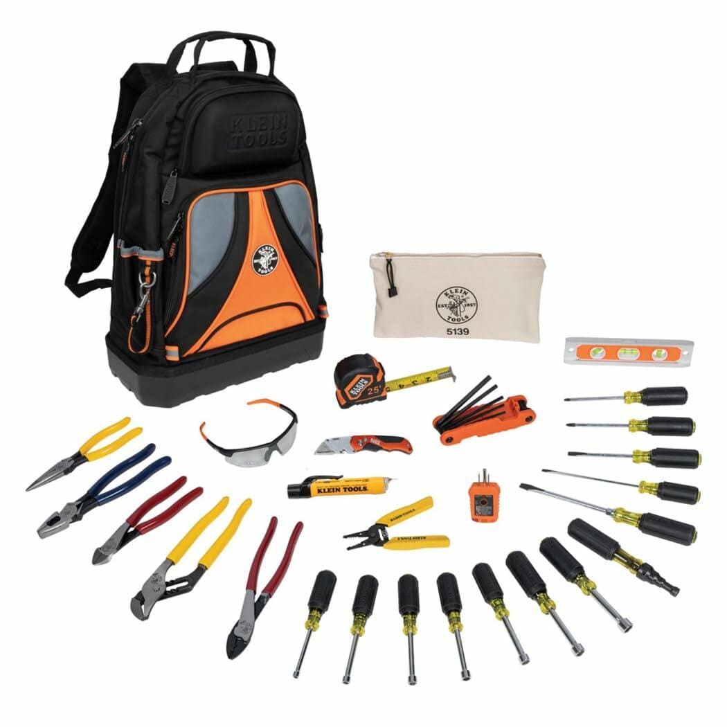 Full Klein Tools 28-piece hand tool kit displayed in front of branded backpack, including pliers, screwdrivers, testers, tape measure, level, and safety glasses.