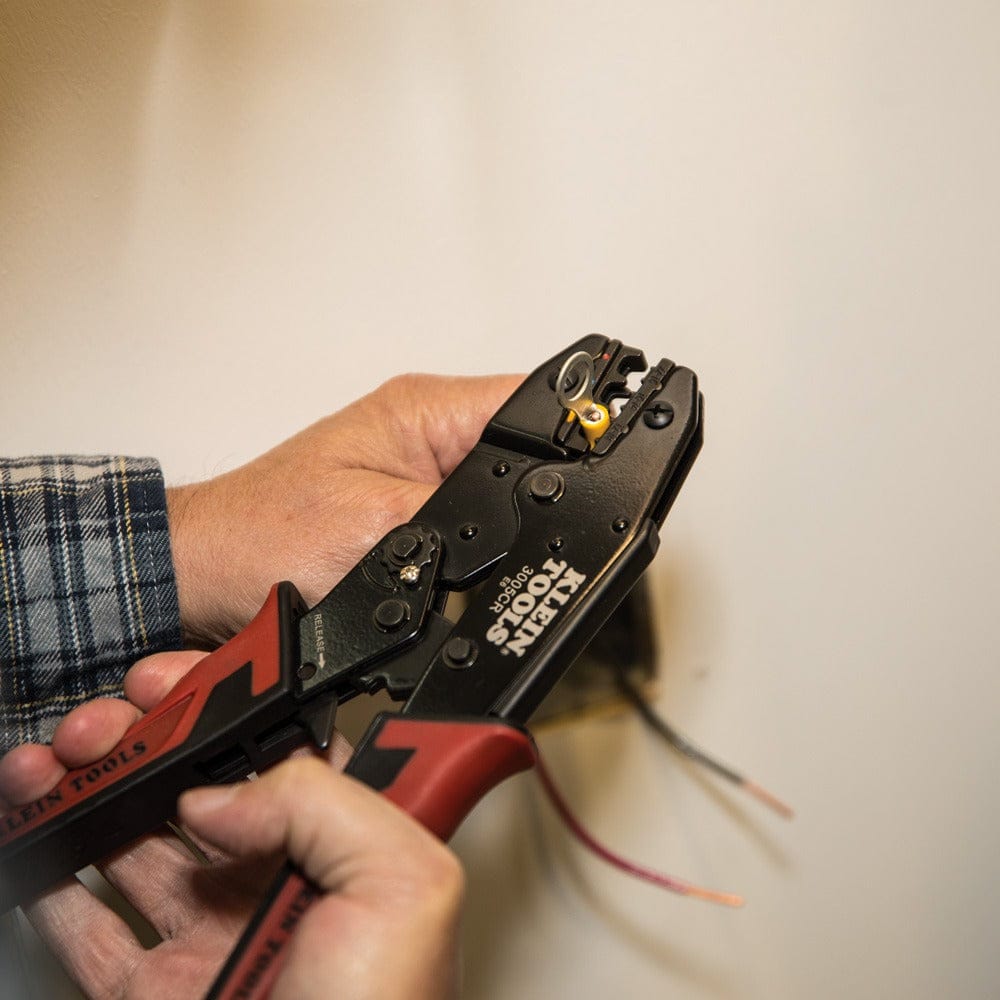 A close-up action shot of a technician using the ratcheting crimper to secure a yellow insulated ring terminal onto the end of a copper wire.
