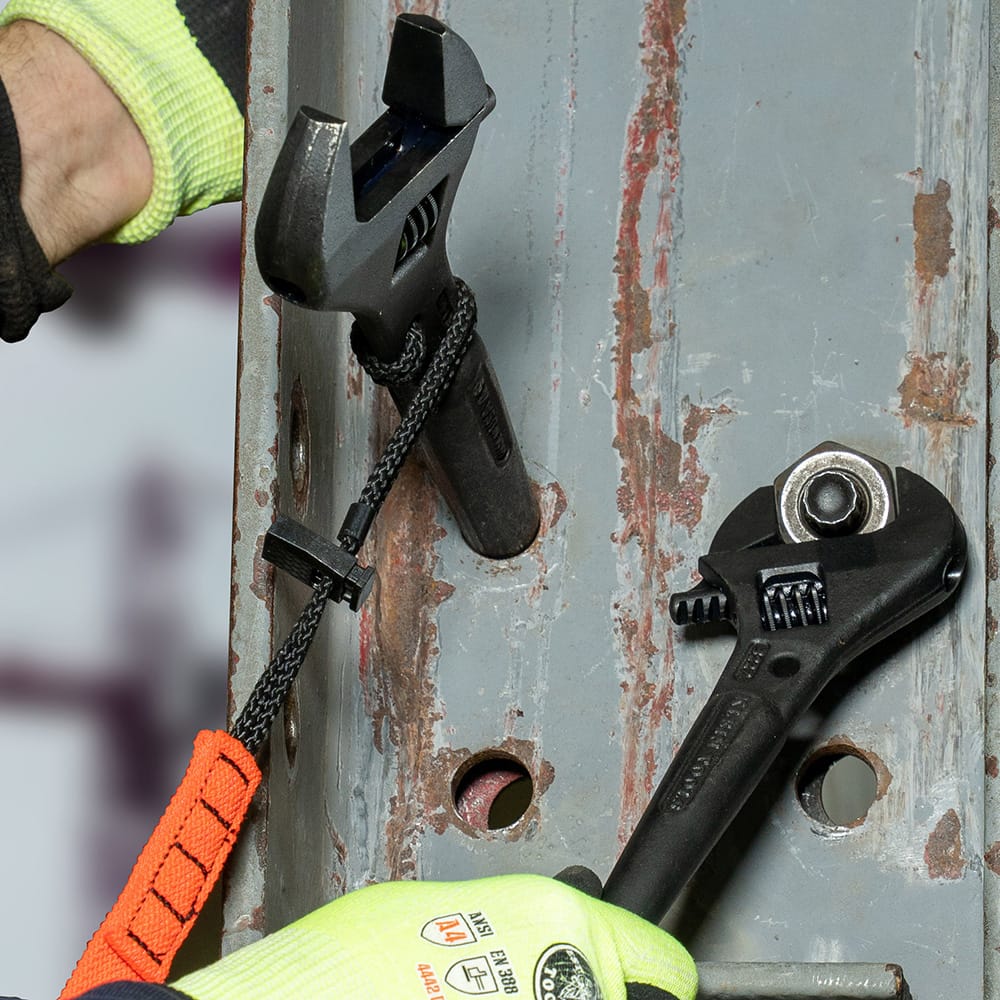 Worker using a Klein Tools 3227 Adjustable Spud Wrench with tether cord attached to prevent drops while aligning bolts on a steel beam in a construction environment.