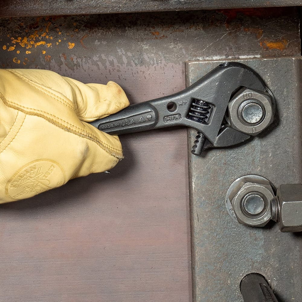 Gloved hand tightening a large bolt with a Klein Tools 3227 Adjustable Spud Wrench marked Made in USA, used for heavy‑duty industrial and construction maintenance.