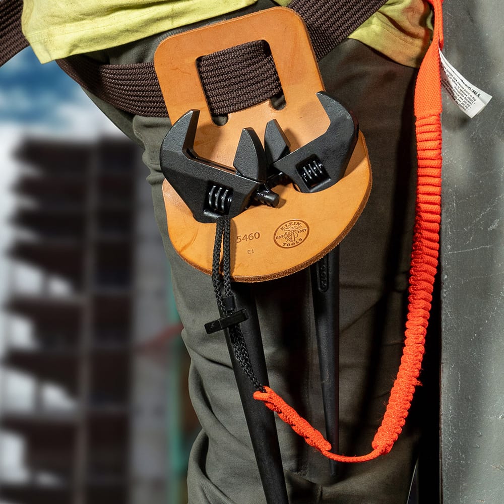 Tool belt holding Klein Tools adjustable spud wrenches and pliers secured with safety lanyards, demonstrating tether‑ready setup for construction or work‑at‑height environments.