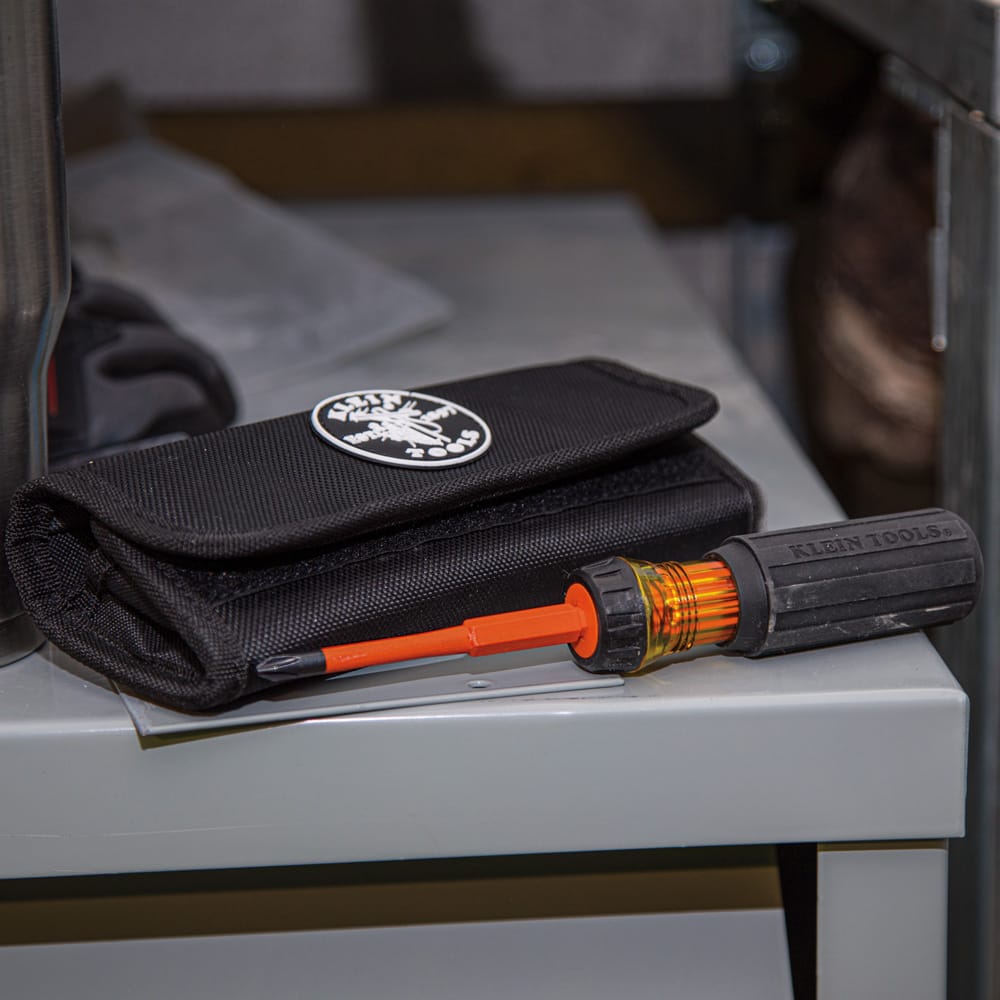Klein Tools 32288 8-in-1 insulated interchangeable screwdriver set close up view featuring a black rubberized Cushion-Grip handle with an amber-colored locking collar and an orange blade locked in place, resting on a gray metal surface next to its matching black storage roll pouch with a circular brand patch.