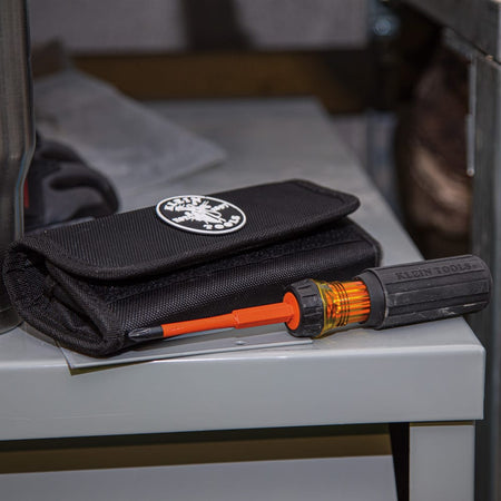 Klein Tools 32288 8-in-1 insulated interchangeable screwdriver set close up view featuring a black rubberized Cushion-Grip handle with an amber-colored locking collar and an orange blade locked in place, resting on a gray metal surface next to its matching black storage roll pouch with a circular brand patch.