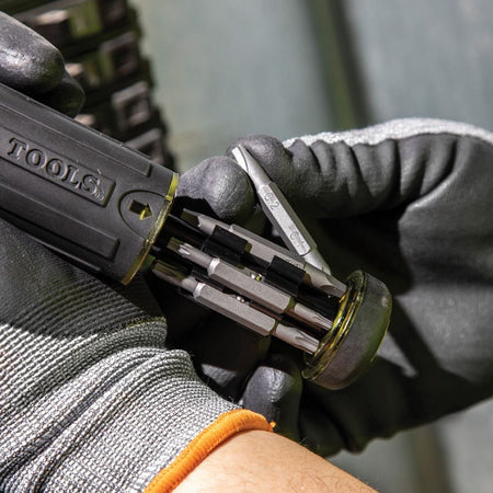 A gloved hand removing a double-ended bit from the pull-out storage canister located in the screwdriver handle.