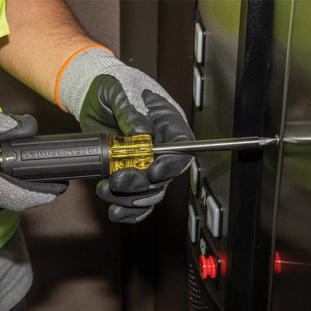 An action photograph of a professional using the Klein 32307 tamperproof screwdriver to service a secure elevator control panel, highlighting the tool's effectiveness on specialty security fasteners.