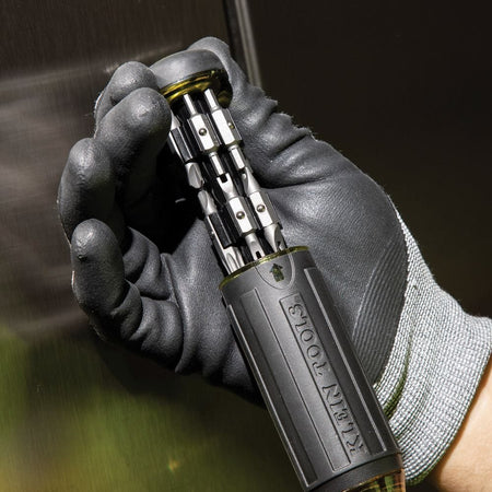 A close-up action shot showing a professional's gloved hand holding the Klein 32307 screwdriver with the bit storage compartment extended, ready for a specialty bit change.