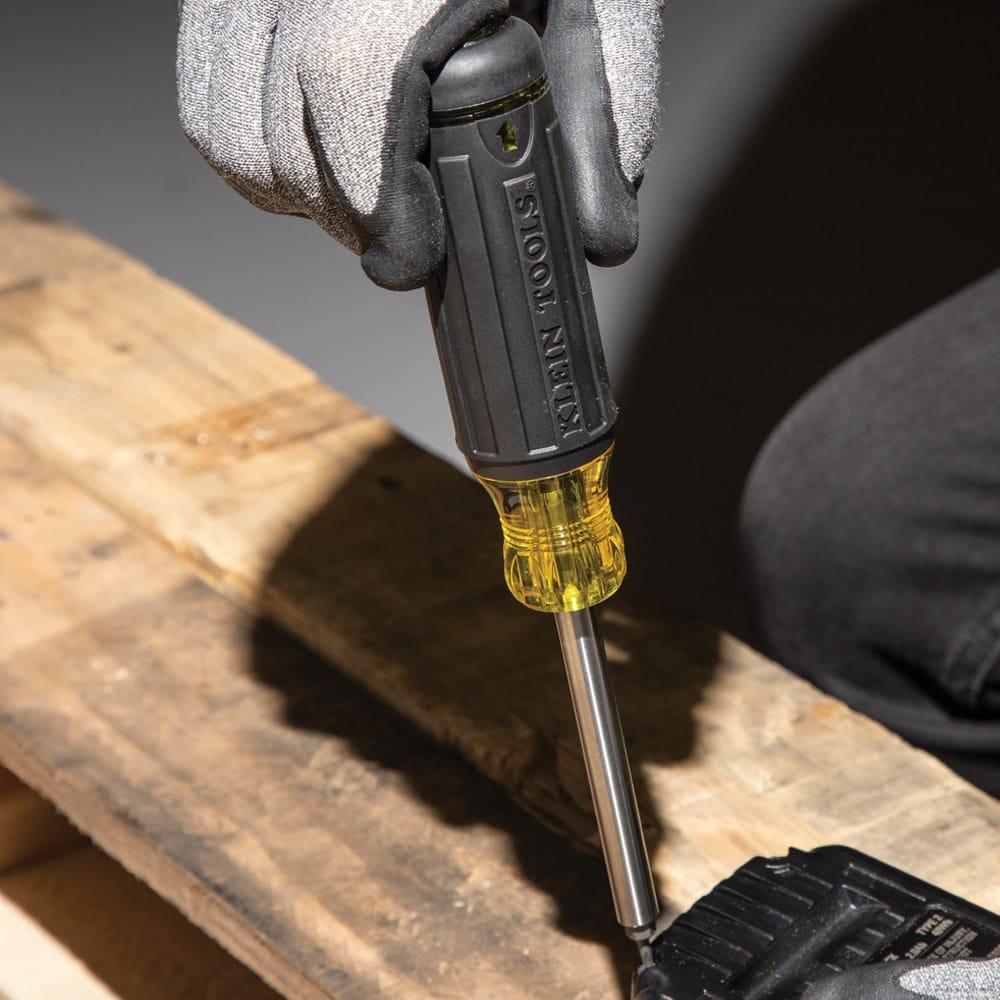 A tradesperson using the Klein Tools 32307 27-in-1 driver to fasten a security screw on a piece of equipment, demonstrating the precision and high-torque capability of the Cushion-Grip handle.