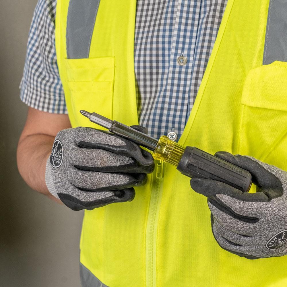 A person wearing a high-visibility safety vest and work gloves holds a Klein Tools multi-bit screwdriver to demonstrate bit installation.