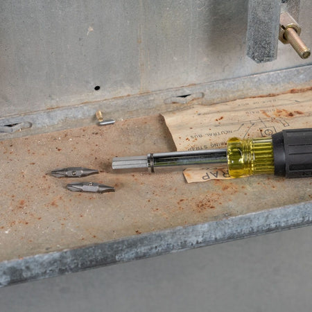 Two double-sided replacement bits sitting inside a metal electrical box next to a multi-bit screwdriver handle.