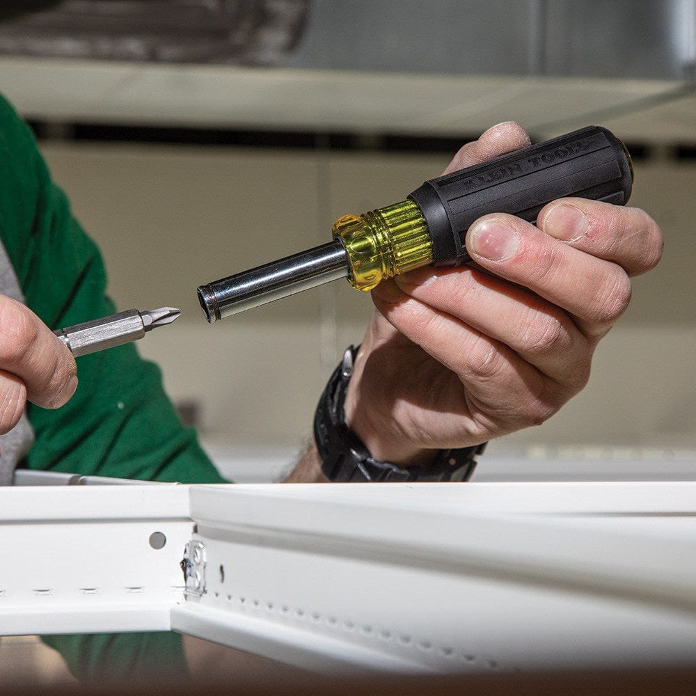 A detailed view of a worker’s hands inserting a double-ended screwdriver bit into the magnetic barrel of the Klein Tools multi-bit driver.