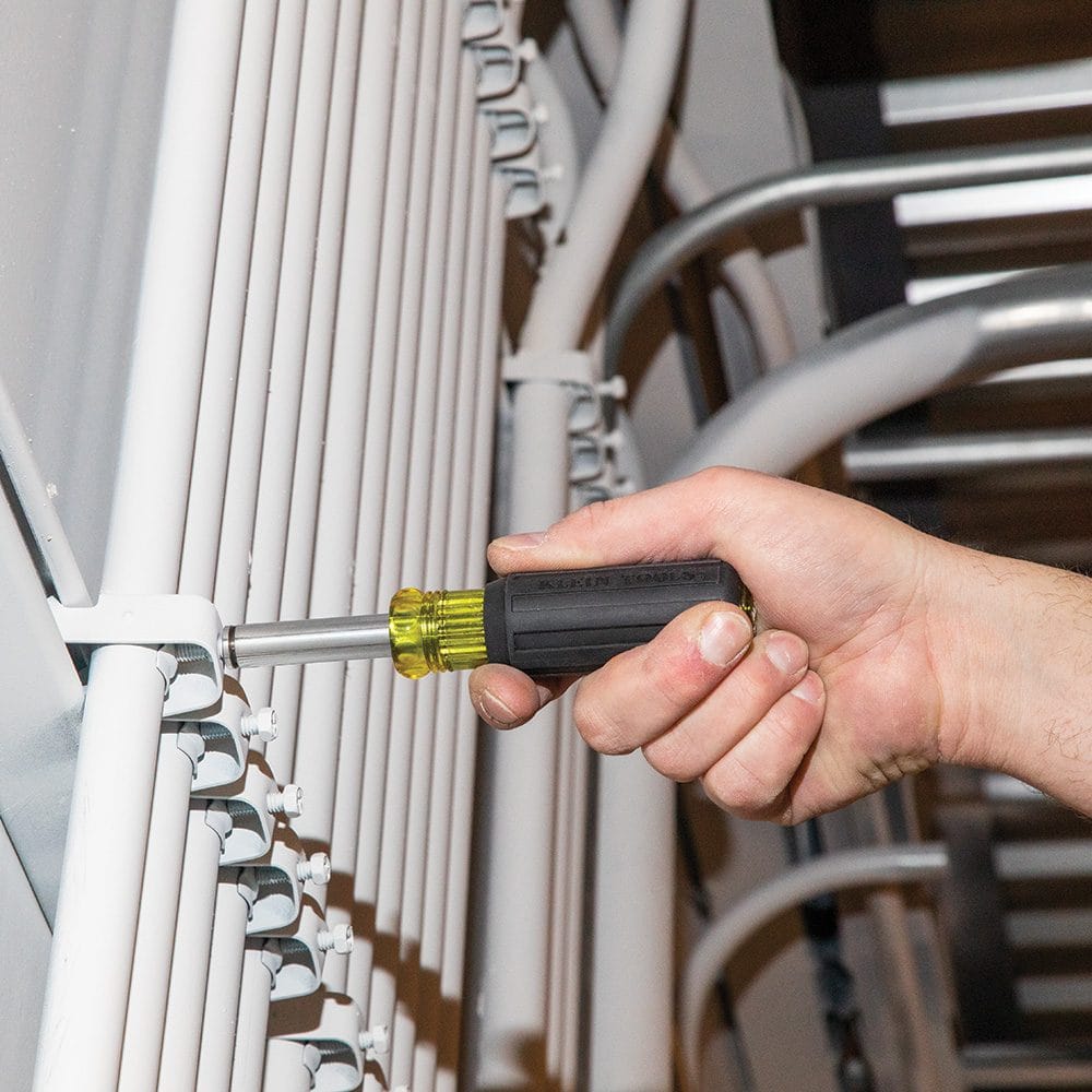 An action shot of the 32500MAG multi-bit driver being used to fasten a metal conduit strap to a vertical white wall.