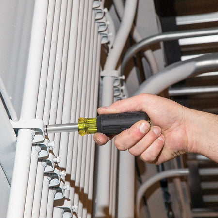 An action shot of the 32500MAG multi-bit driver being used to fasten a metal conduit strap to a vertical white wall.