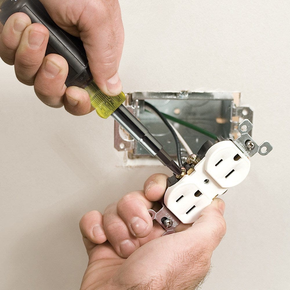 A close-up action shot of the 11-in-1 driver being used to secure terminal screws on a duplex electrical outlet during installation in a metal junction box.