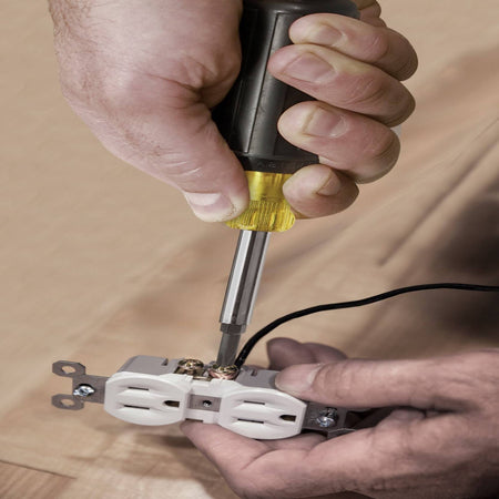 An action photo showing the multi-tool being used to fasten a wire to an electrical outlet, emphasizing the precision and control of the Cushion-Grip handle.