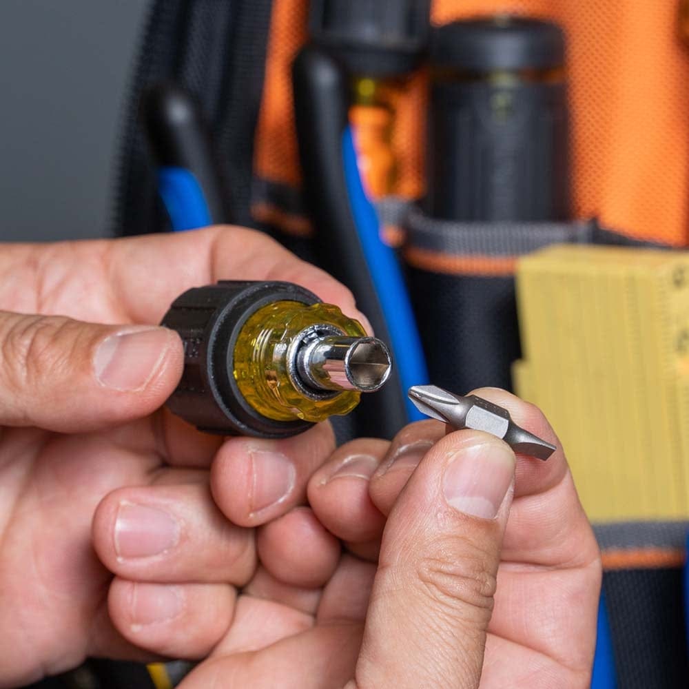 Close-up of hands holding the stubby screwdriver handle and shaft while positioning a Phillips head bit for insertion into the nut driver end.