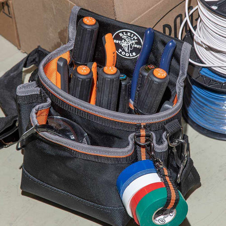 A professional black and orange tool pouch filled with Klein insulated screwdrivers and electrical tools, showcasing the 33734INS set stored alongside electrical tape and pliers for quick jobsite access.