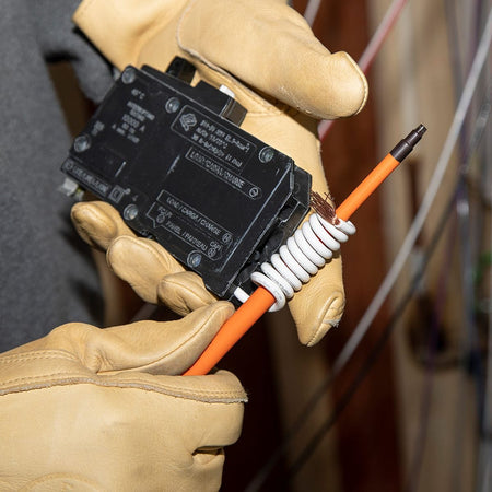 A close-up action view of a technician wearing protective tan leather gloves using a Klein Tools slim-tip insulated square-drive screwdriver to wire a commercial circuit breaker, demonstrating how the flush orange dielectric insulation safely passes into deep wire clamp ports without chipping.