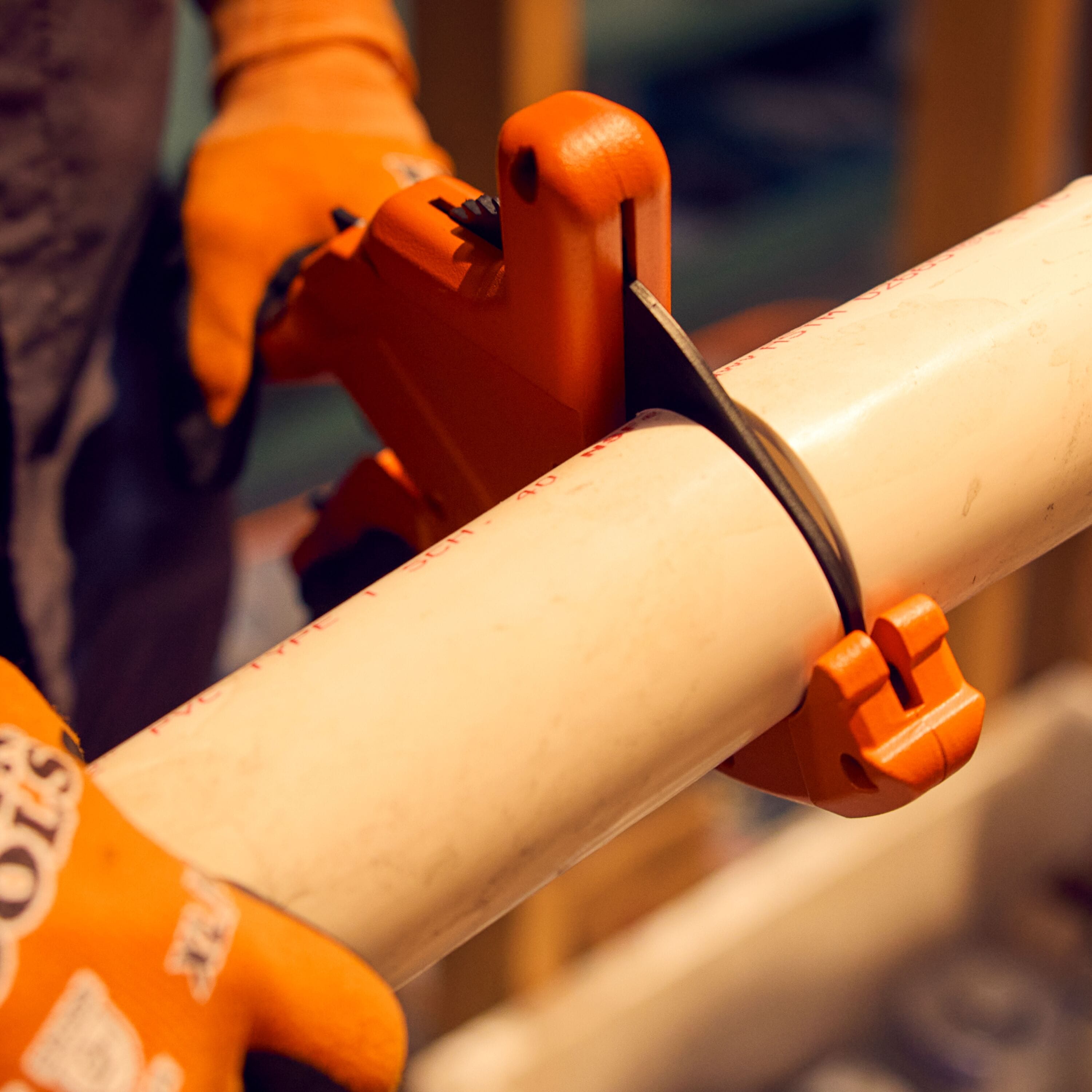 A close-up field action perspective of a contractor using the high-leverage mechanical ratcheting blade of the heavy-duty Klein pipe cutter to step down through a thick-walled white PVC plumbing line, highlighting square edge tracking and professional jobsite execution.