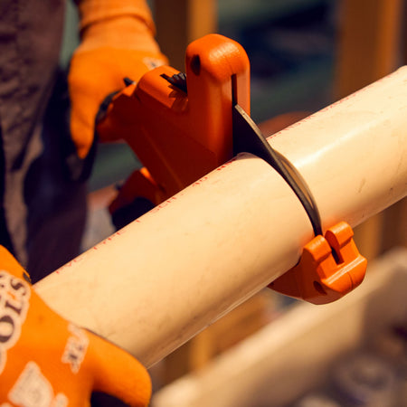 A close-up field action perspective of a contractor using the high-leverage mechanical ratcheting blade of the heavy-duty Klein pipe cutter to step down through a thick-walled white PVC plumbing line, highlighting square edge tracking and professional jobsite execution.
