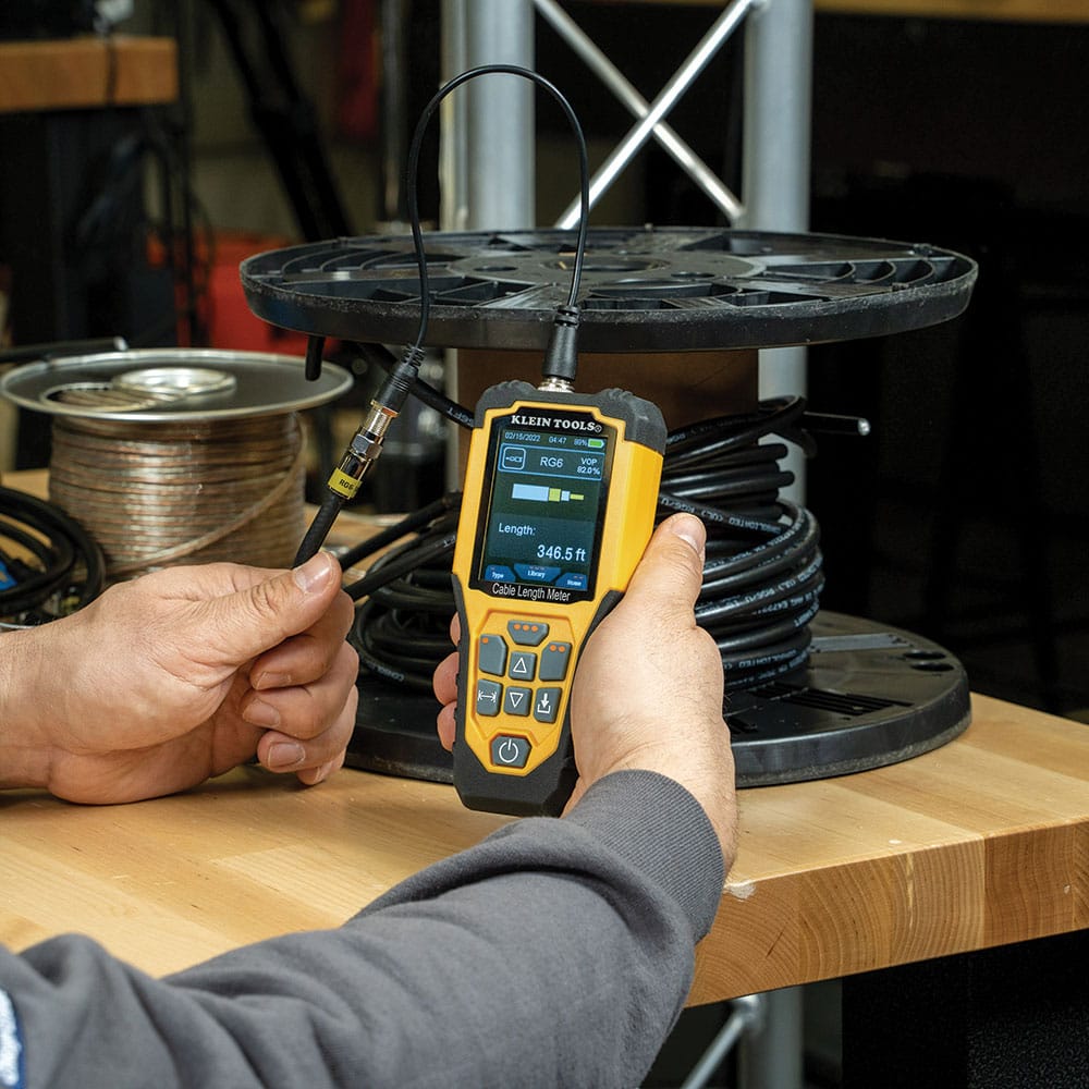 Action shot of a professional measuring a bulk spool of RG6 coaxial cable using the 501915 TDR meter. The device displays a length of 346.5 feet, demonstrating how the Time Domain Reflectometry technology provides instant verification of remaining cable on industrial spools.