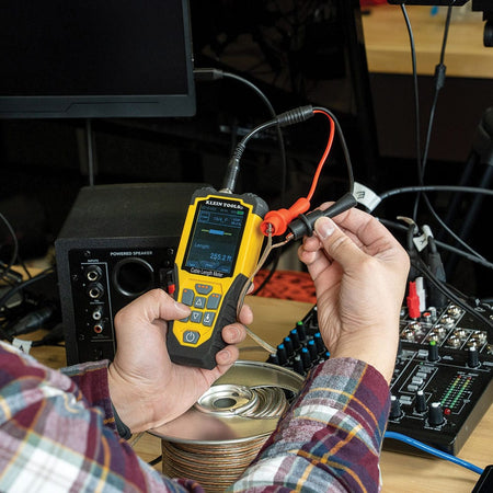 Action shot of a professional technician using the 501915 TDR meter to measure the length of a high-fidelity speaker wire. The color LCD display shows a precise distance reading of 255.2 feet, illustrating the tool's effectiveness for residential and commercial audio-visual wire management.